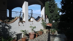 Un espace extérieur abrité, doté d’un sol en pierre, de plantes en pot et d’une rambarde.