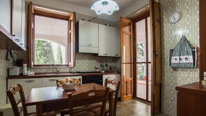 Une cuisine avec des meubles de rangement en bois, une table à manger avec des chaises, une fenêtre et une horloge au mur.