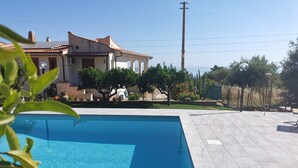 Une piscine dotée d’une terrasse carrelée, entourée d’un jardin et d’une maison dont le toit est également recouvert de tuiles.
