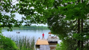 A wooden dock leading to a boat, surrounded by dense greenery and a calm lake. - Just a fishing cabin in the woods... (Portland)