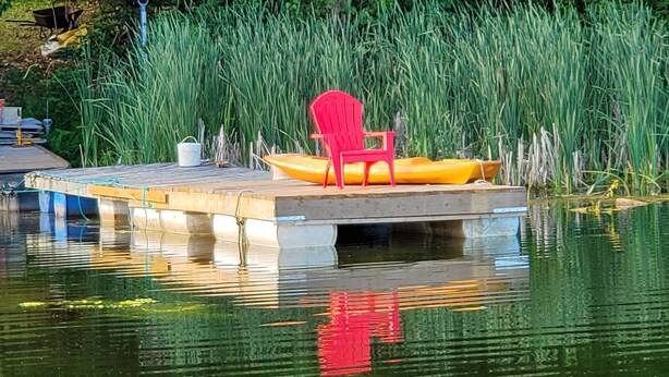 A dock with a red chair and a yellow boat, surrounded by tall green grass. - Just a fishing cabin in the woods... (Portland)