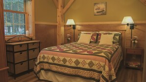 A cozy bedroom with a wooden ceiling, a large bed with a quilt, two bedside lamps, a nightstand, and a dresser. - Immaculate mountain cabin with awe inspiring sunrise and mountain views (Ripton)