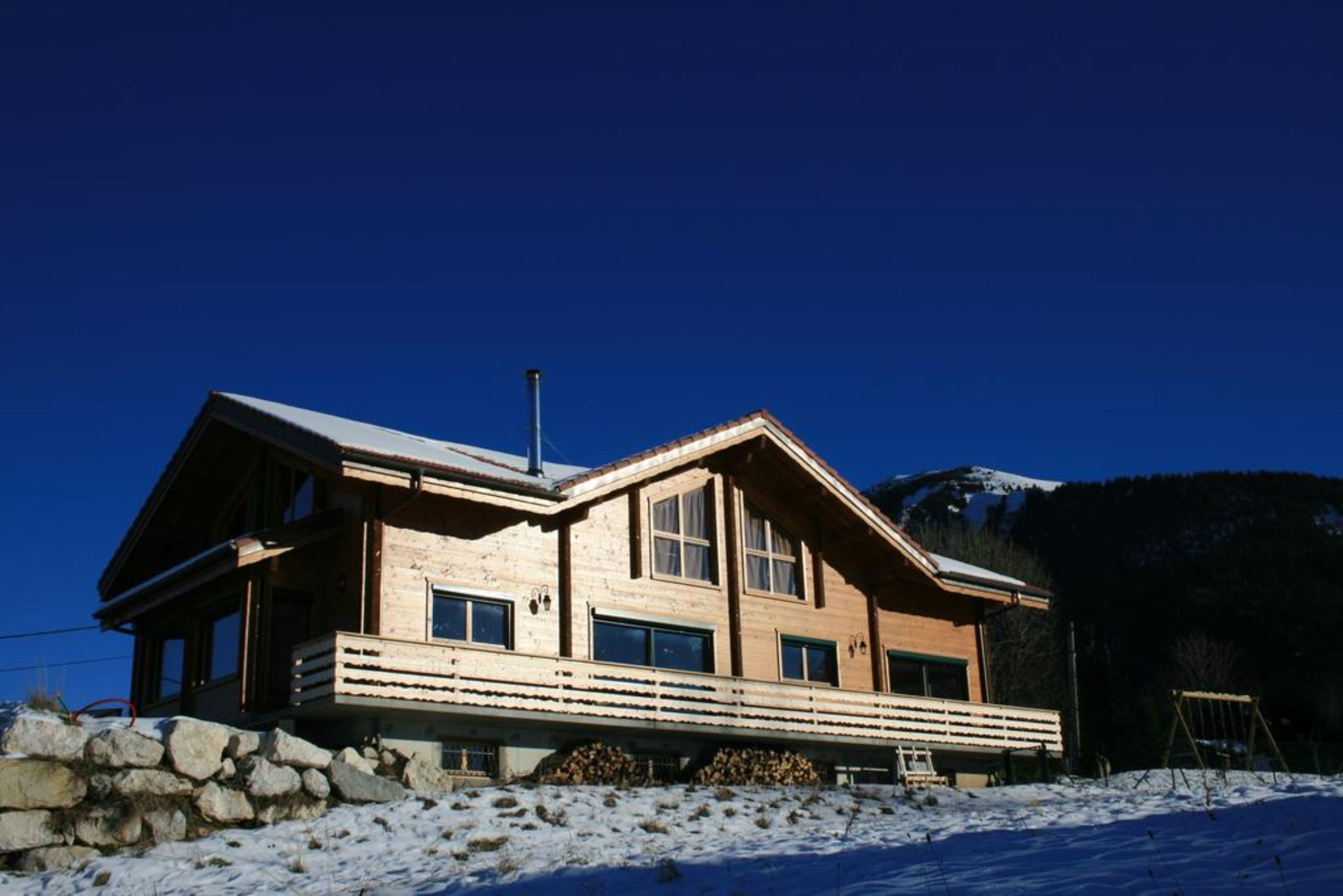Un chalet en bois, avec des fondations en pierre, de grandes fenêtres et un toit en pente.