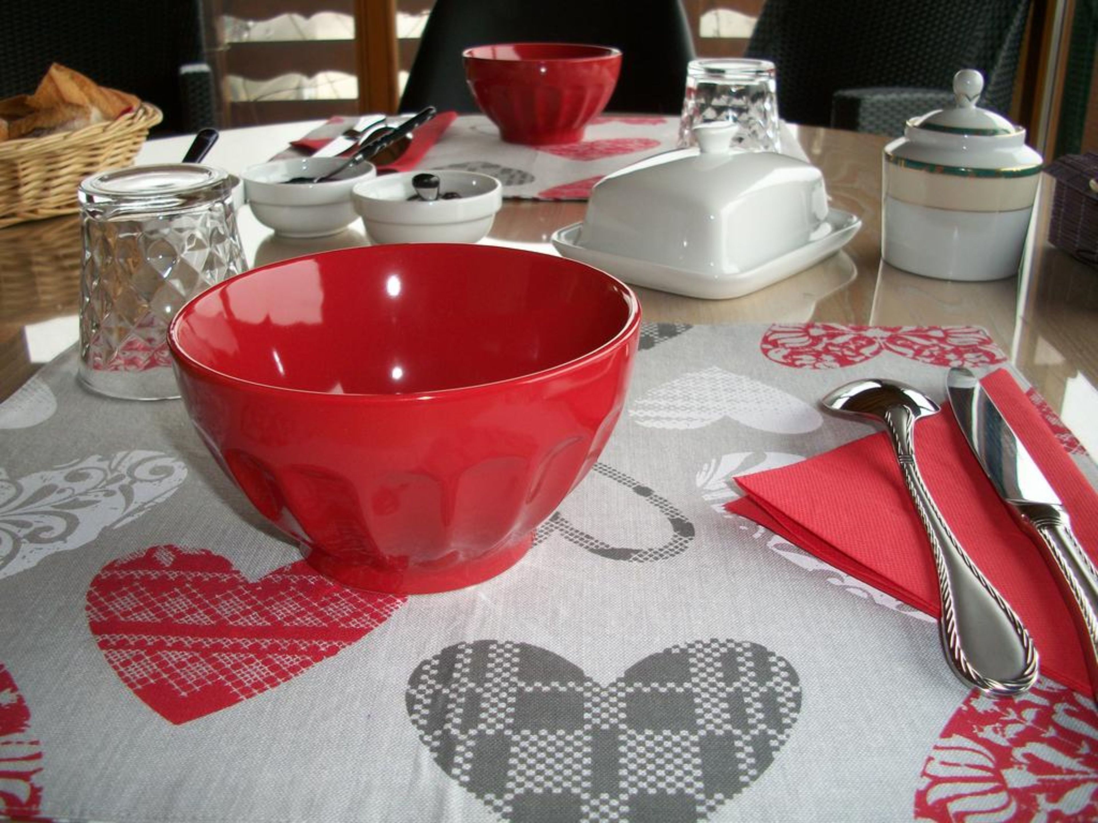 A dining table with a red bowl, silverware, and a patterned tablecloth.