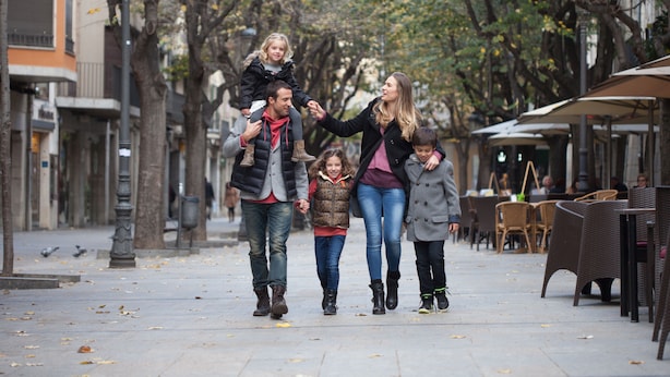 Una familia caminando por una acera bordeada de árboles.