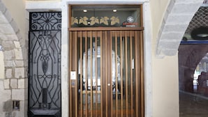 Un portón de madera con un diseño decorativo de metal, un letrero encima y una pared de piedra a la izquierda.