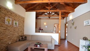 Un salón con techo de madera, un sofá, una mesa de centro y una cocina al fondo.