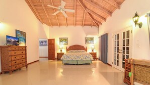 Une chambre à coucher comprenant un lit, une commode en bois, un ventilateur de plafond et des lampes fixées au mur.