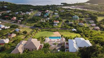 An aerial view of a residential area with houses, a swimming pool, and a beach.