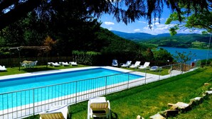Piscina rectangular con barandilla metálica, rodeada de sillas reclinables blancas y un césped.