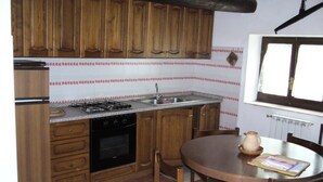 Una cocina con armarios de madera, estufa a gas, lavamanos y una mesa de comedor con sillas.