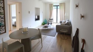 A modern living room with a round dining table, two sofas, a TV mounted on the wall, and a balcony with curtains. - Comfort apartment, warmth in the center of Girona. WIFI & AIR. (Girona)