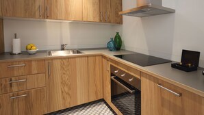 A modern kitchen with wooden cabinets, a stainless steel sink, a black induction cooktop, and a built-in oven. - Comfort apartment, warmth in the center of Girona. WIFI & AIR. (Girona)