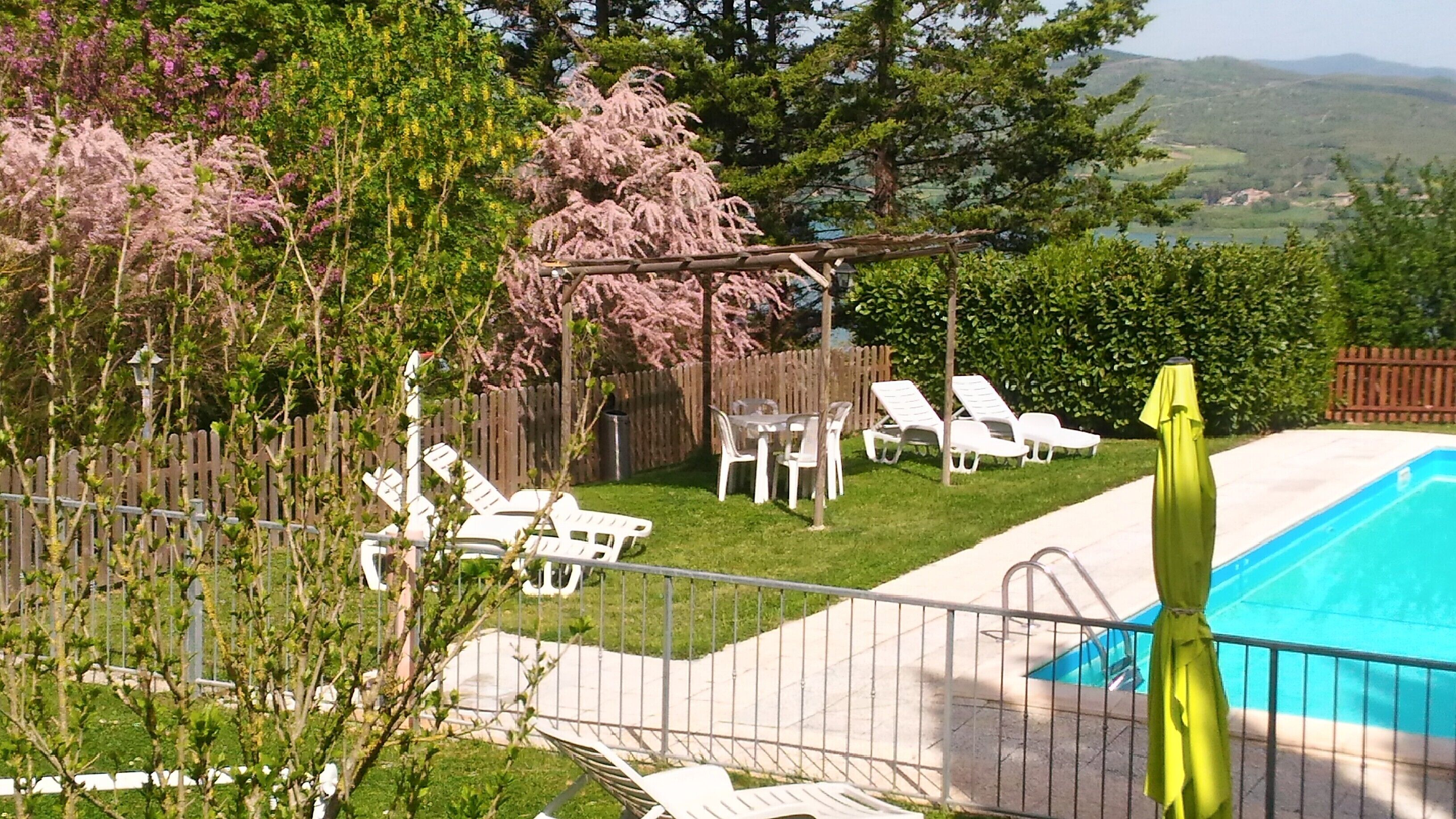 A backyard with a swimming pool, white lounge chairs, and a wooden deck.
