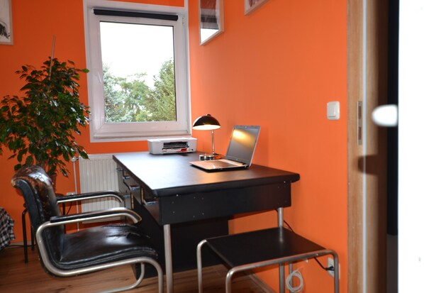 A room with an orange wall, a window, a desk with a laptop, a chair, and a radiator.