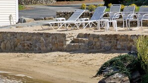 Zona de playa con sillas reclinables blancas y un muro de piedra.