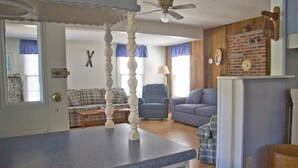 Una sala de estar con sofá, sillones y una mesa de comedor. Hay una chimenea con pared de ladrillo y un reloj.