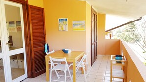 A balcony with a wooden table and chairs, a small shelf with bowls, and two framed pictures on the wall. - Three-room Full Optional Villasimius Country, Climate, Box, Terrace. (Villasimius)