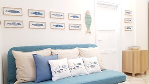 A blue sofa with multiple cushions, a wooden fish decoration on the wall, and a small wooden cabinet with a bowl on top. - Three-room Full Optional Villasimius Country, Climate, Box, Terrace. (Villasimius)