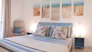 A bedroom with a bed, a chair, a nightstand, and a wall with beach-themed artwork. - Three-room Full Optional Villasimius Country, Climate, Box, Terrace. (Villasimius)
