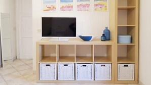 A living room with a TV on a wooden stand, a blue vase, and four wall-mounted paintings. - Three-room Full Optional Villasimius Country, Climate, Box, Terrace. (Villasimius)