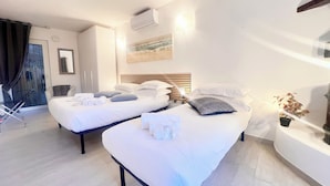 Habitación de hotel con dos camas, una mesita con lámpara, una planta en maceta y una puerta corrediza que da a un balcón.