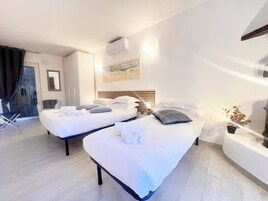 A hotel room with two beds, a small table with a lamp, a potted plant, and a sliding door leading to a balcony.
