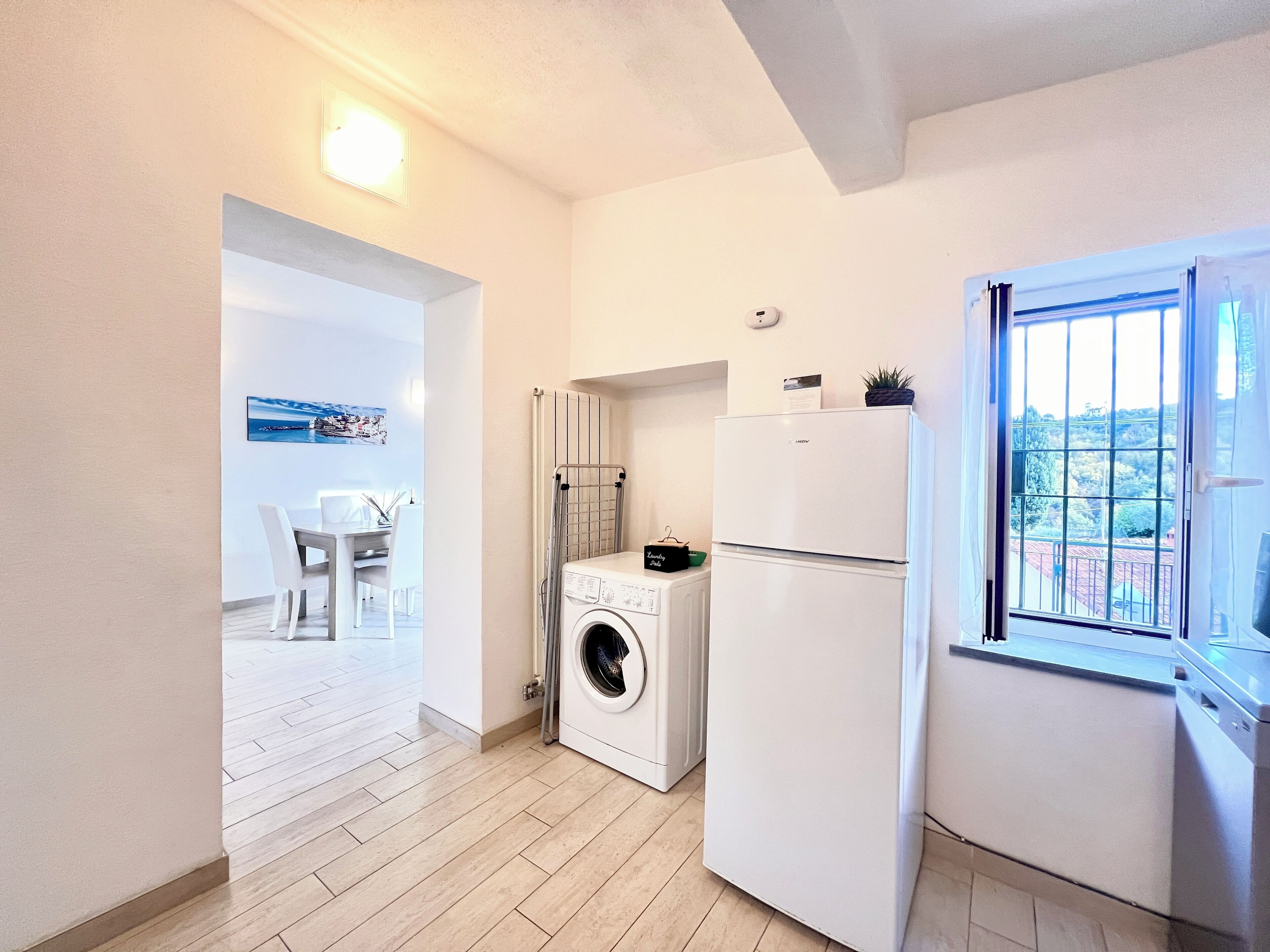 A compact kitchen with a washing machine, a refrigerator, and a window with a view of a hilly landscape.