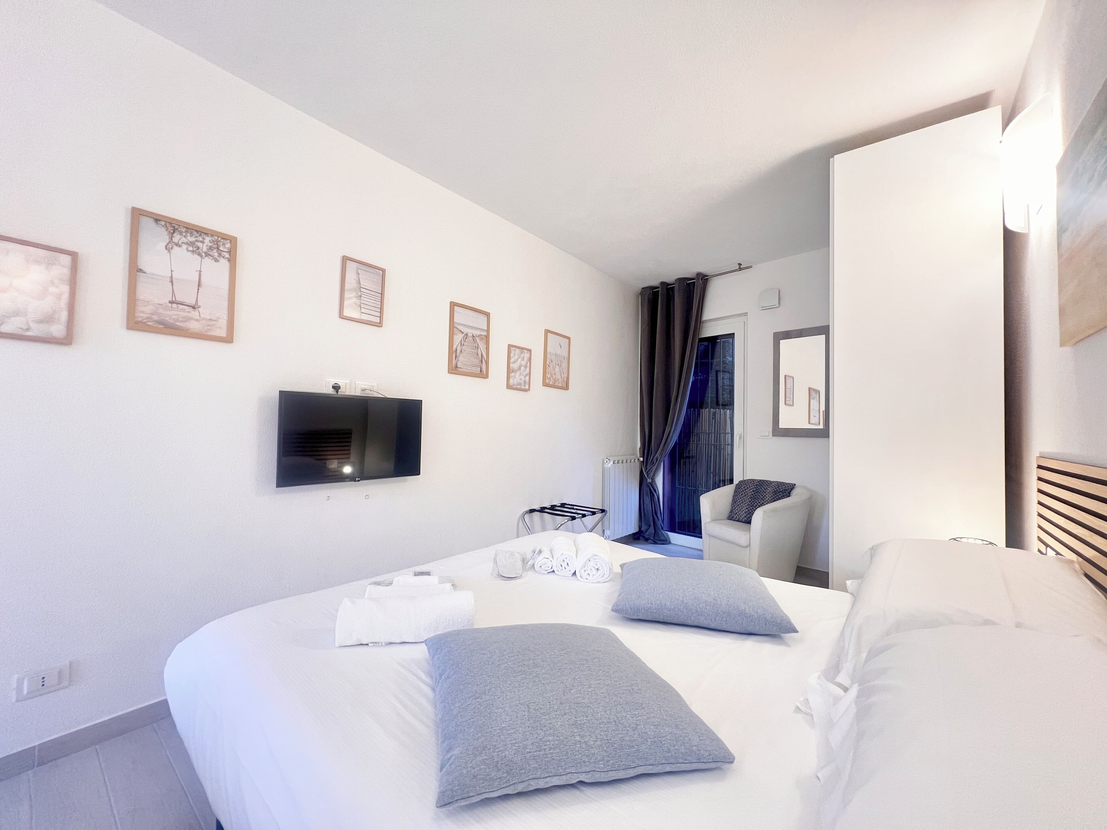 Una moderna camera d'albergo con un letto grande, una TV a schermo piatto montata a parete e una finestra con tende.