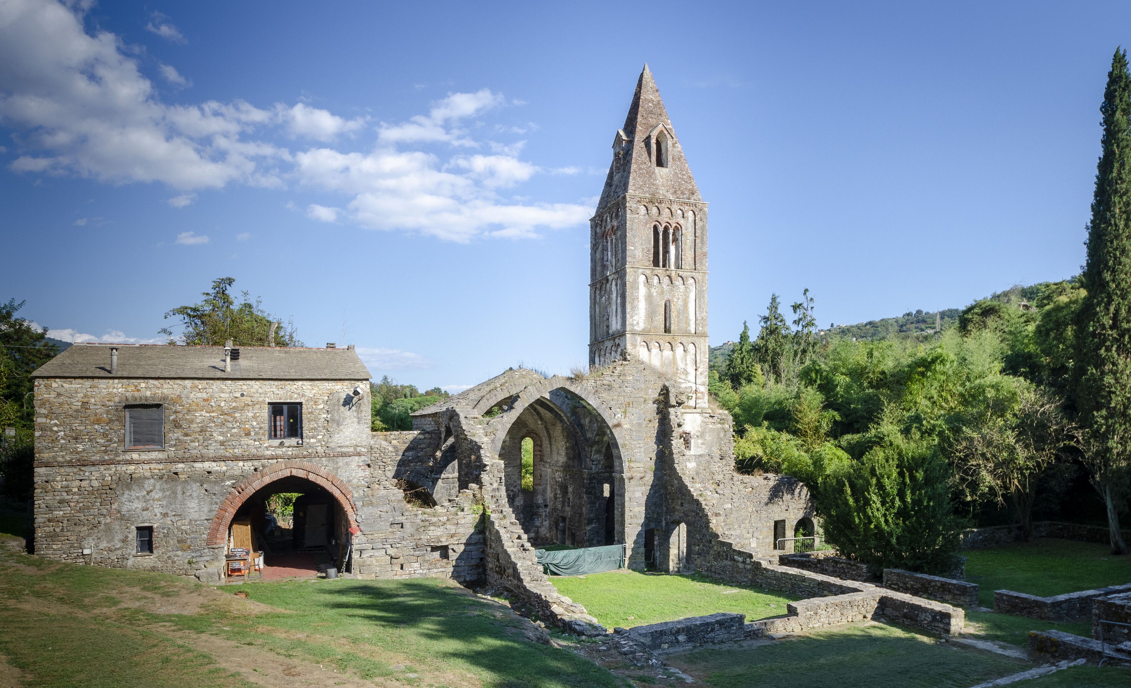 An ancient stone building with a tall tower, arched windows, and a grassy courtyard.