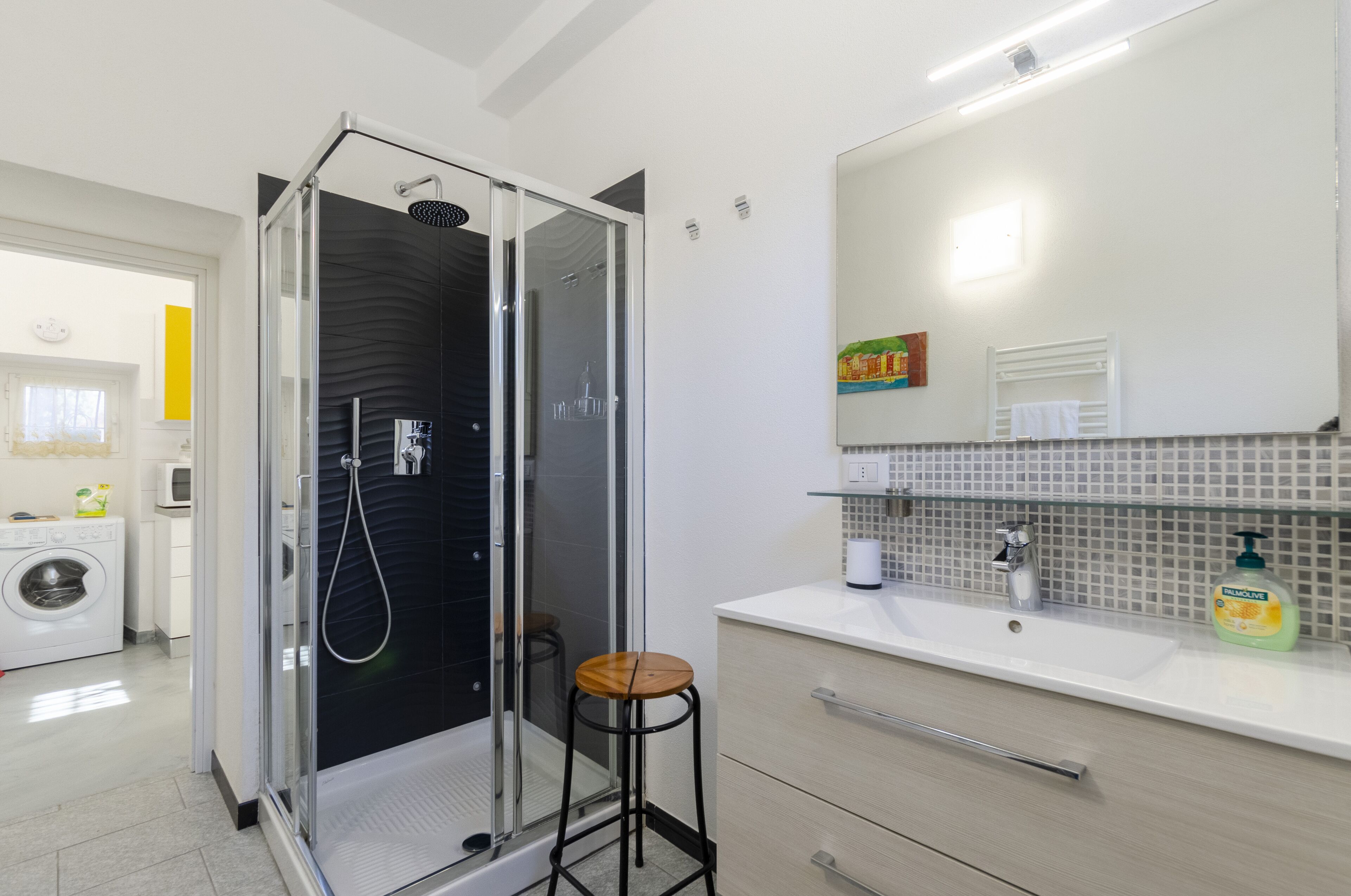 Un baño moderno con ducha de vidrio, un lavabo con espejo y un taburete pequeño.