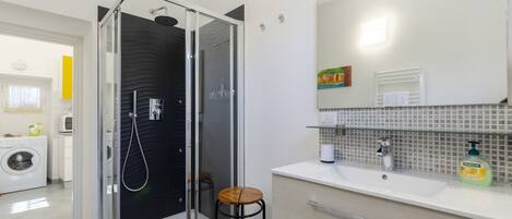 Un baño moderno con ducha de vidrio, un lavabo con espejo y un taburete pequeño.