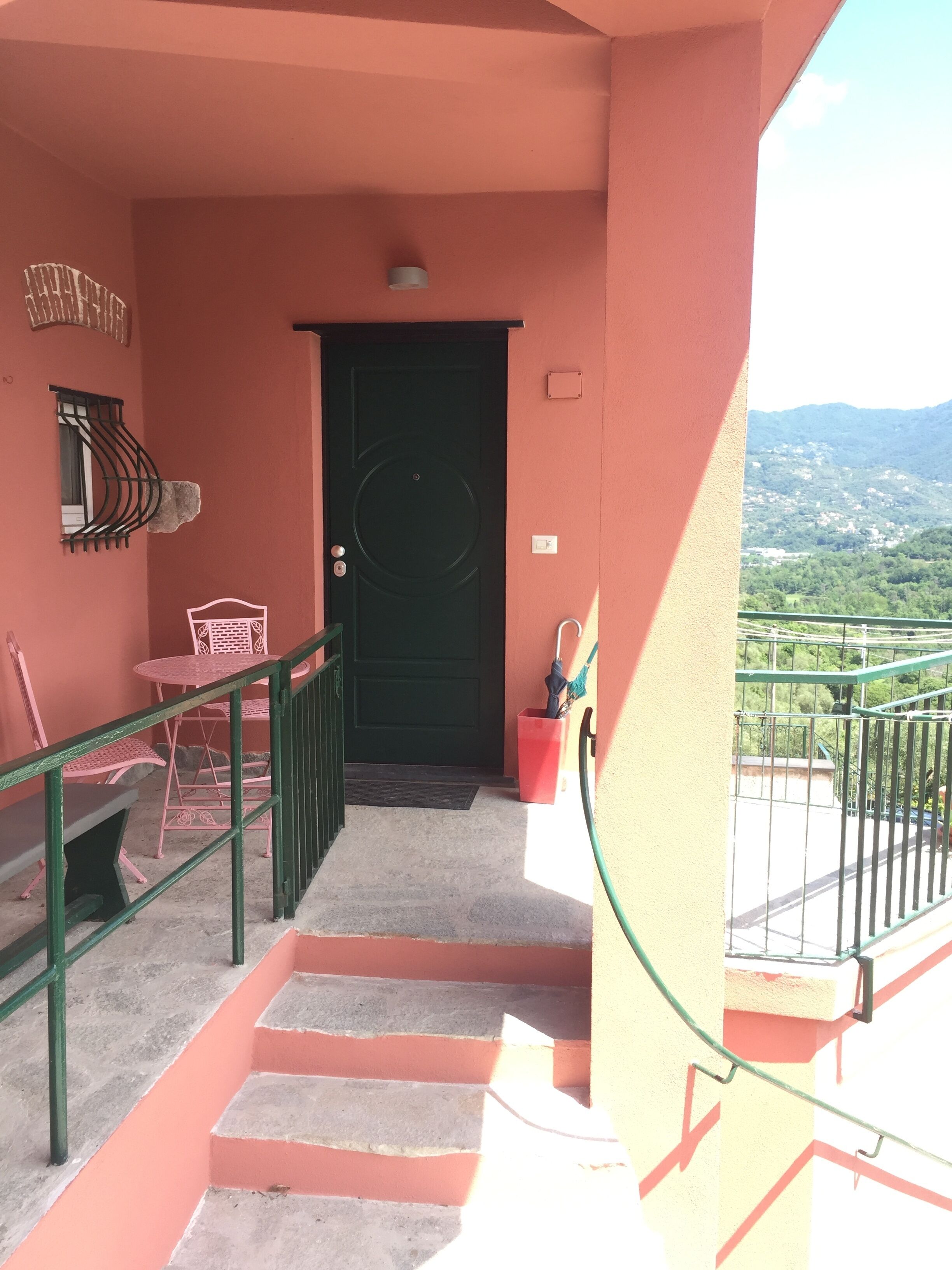 A balcony with a view of a mountainous landscape, a black door, and a small red trash bin.