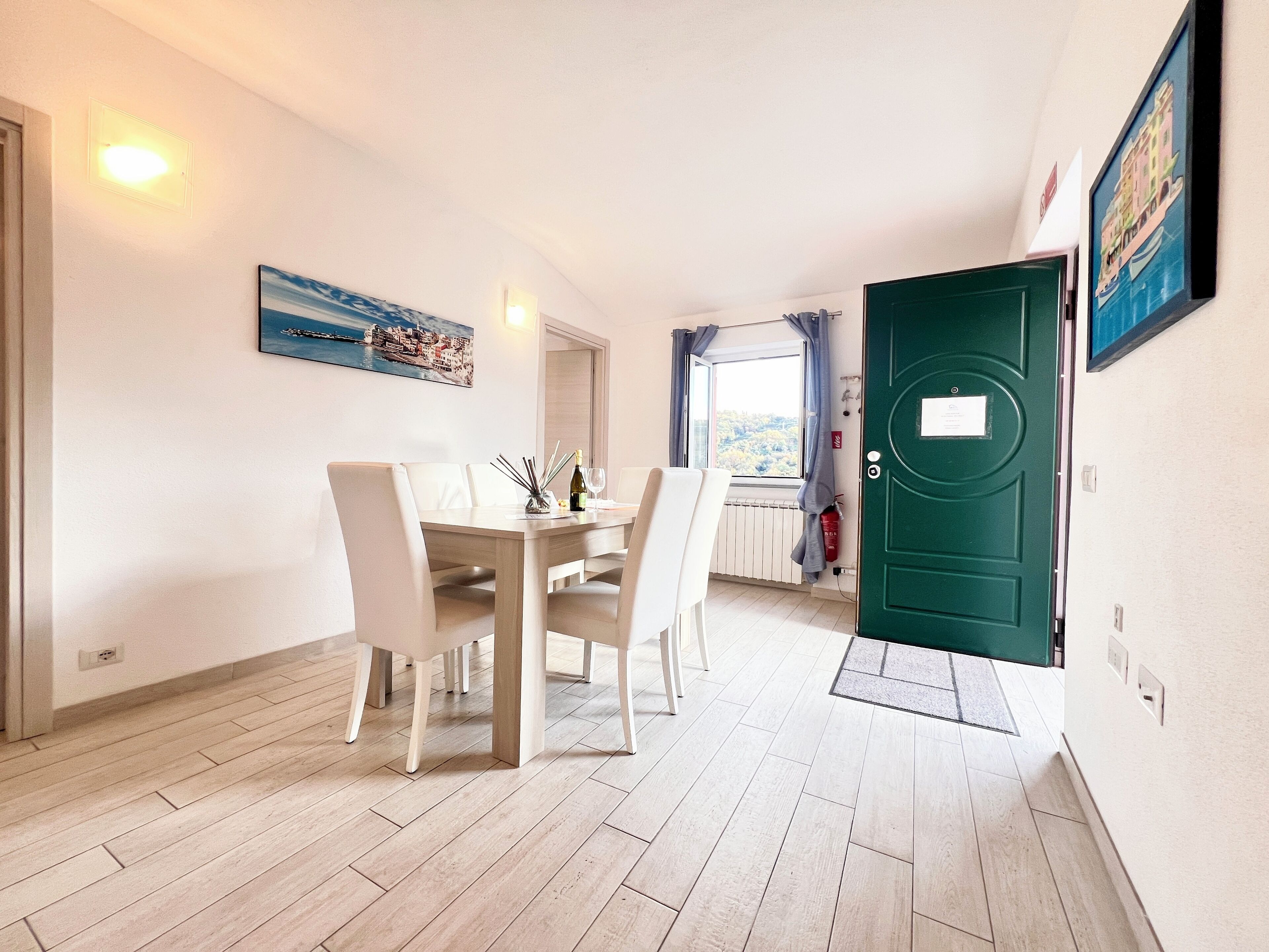 Un comedor con una mesa dispuesta para cuatro, una puerta verde y una ventana con vistas al verdor.