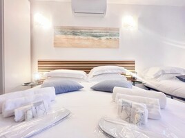 A hotel room with a bed, two bedside tables, a wall-mounted air conditioner, and a painting of a beach scene.