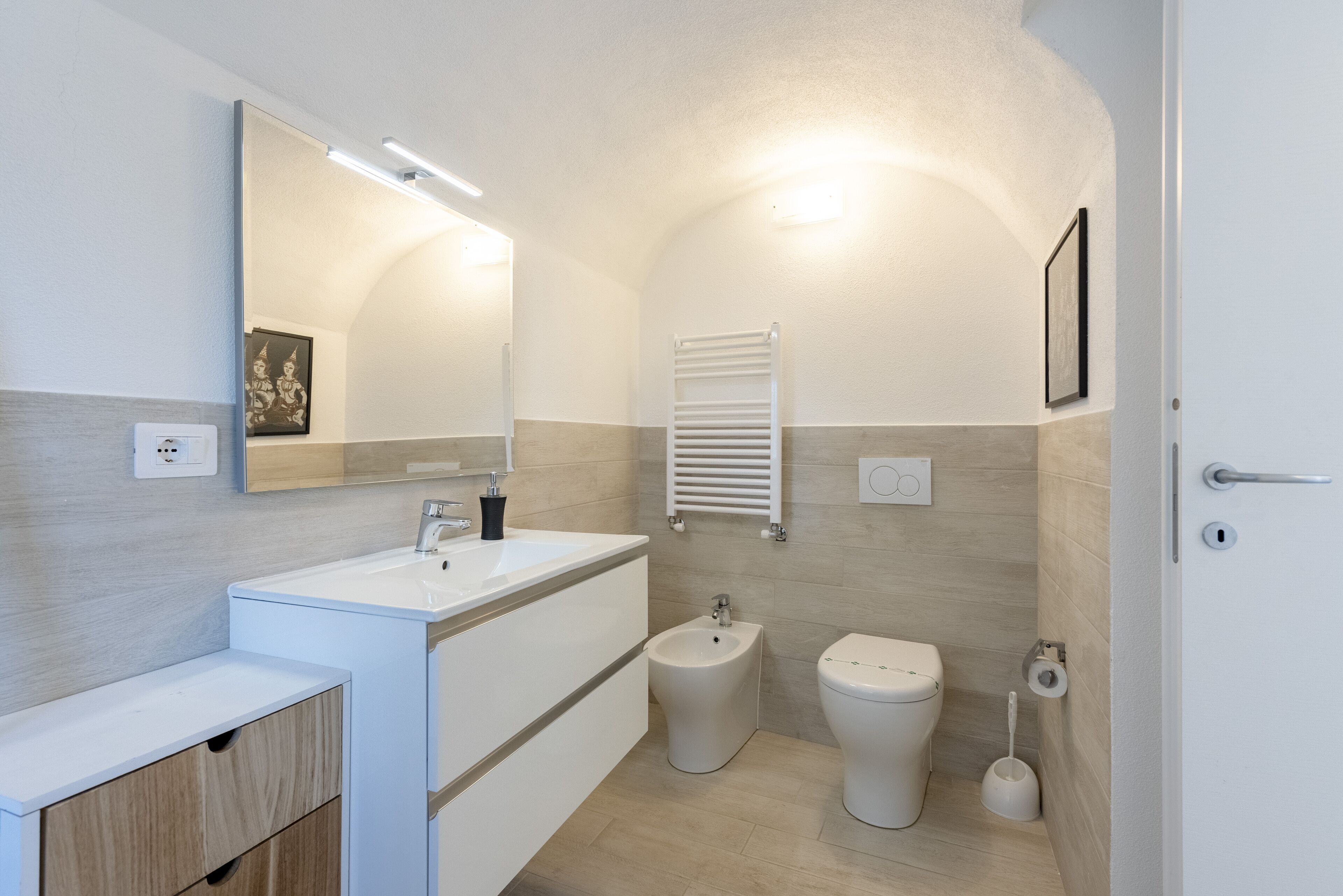 Een moderne badkamer met een witte wastafel, bidet, toilet en een handdoekhouder.