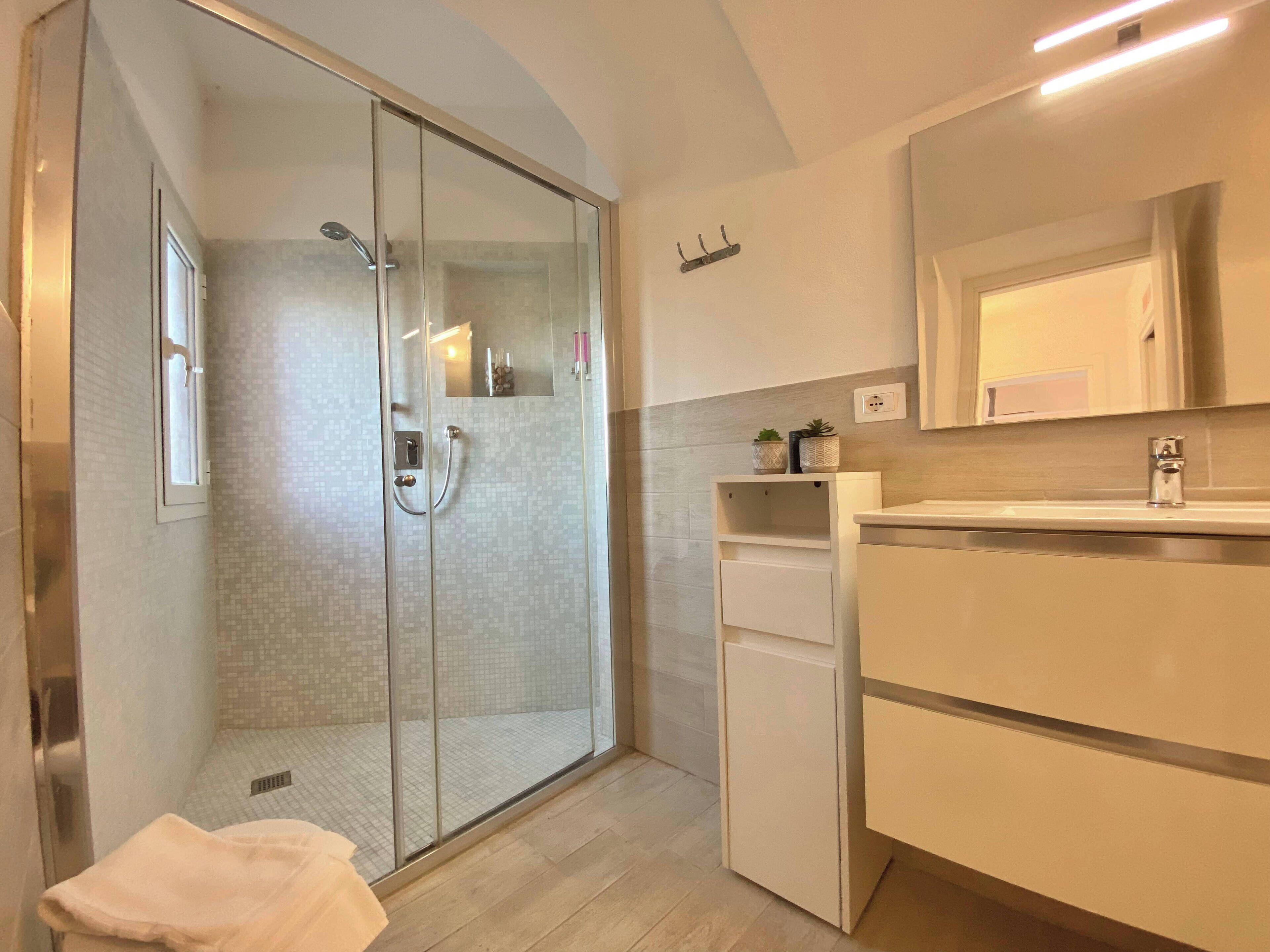 Un bagno moderno con cabina doccia in vetro, lavabo incassato e specchio sopra il piano di lavoro.