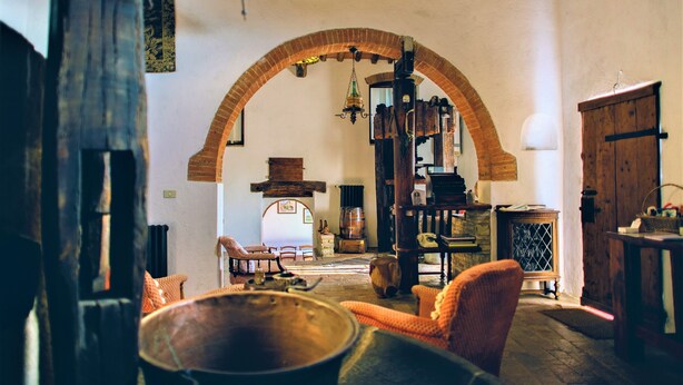 A rustic interior with a large arched doorway, wooden furniture, and a hanging light fixture. - Beautiful apartment in Chianti on organic farm with pool and 360° sunset views (Siena)