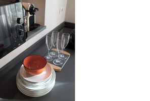 A kitchen counter with a coffee machine, a bottle of wine, and stacked plates and glasses.