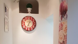 Un couloir avec une horloge murale ronde, une plante en pot et un radiateur.