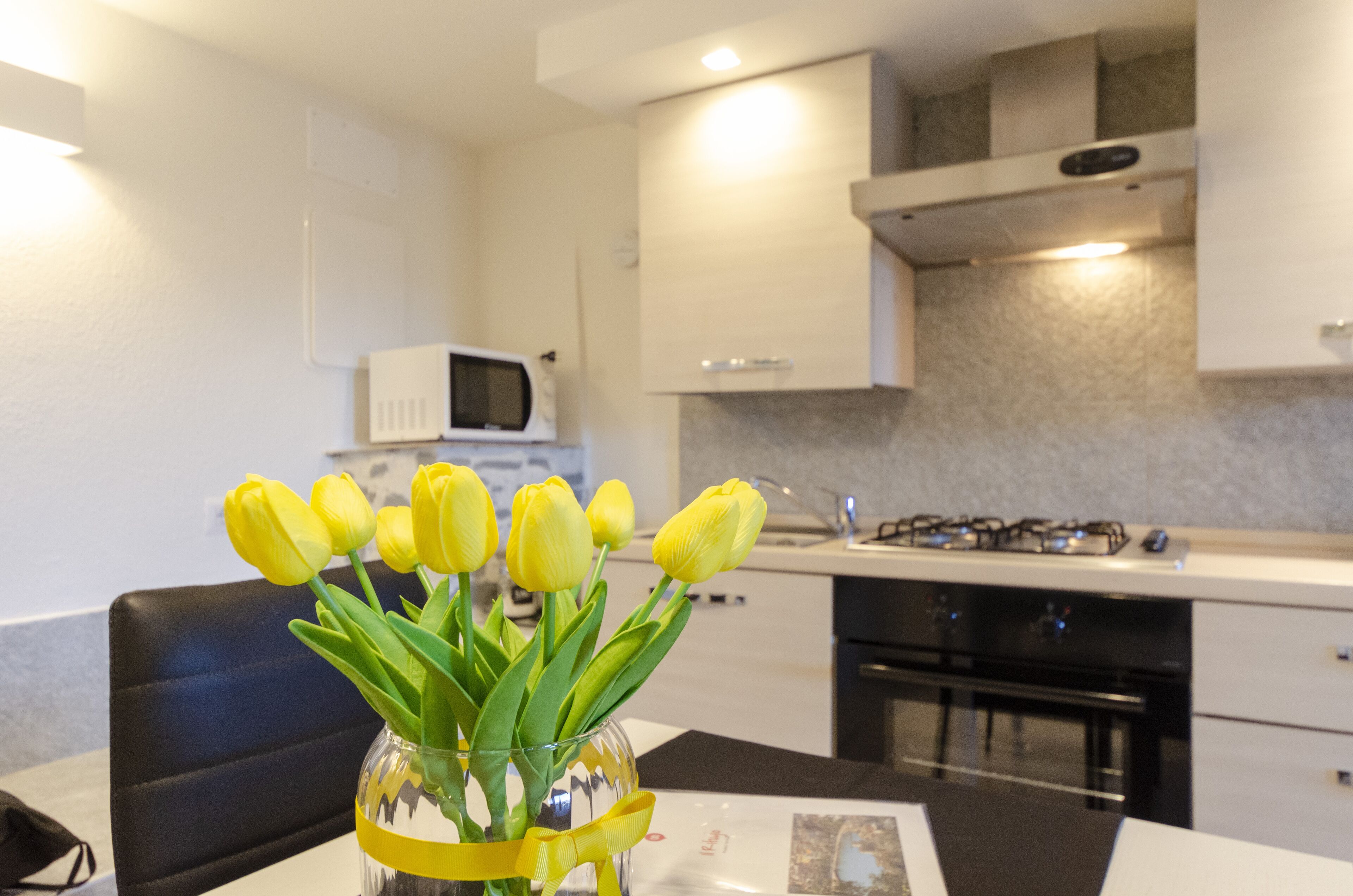 A modern kitchen with white cabinets, a microwave, and a gas stove. There is a vase with yellow tulips on the table.