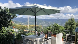An outdoor patio with a table and chairs, an umbrella, and a view of mountains. - Il Rifugio di San Massimo, Rapallo (Rapallo)