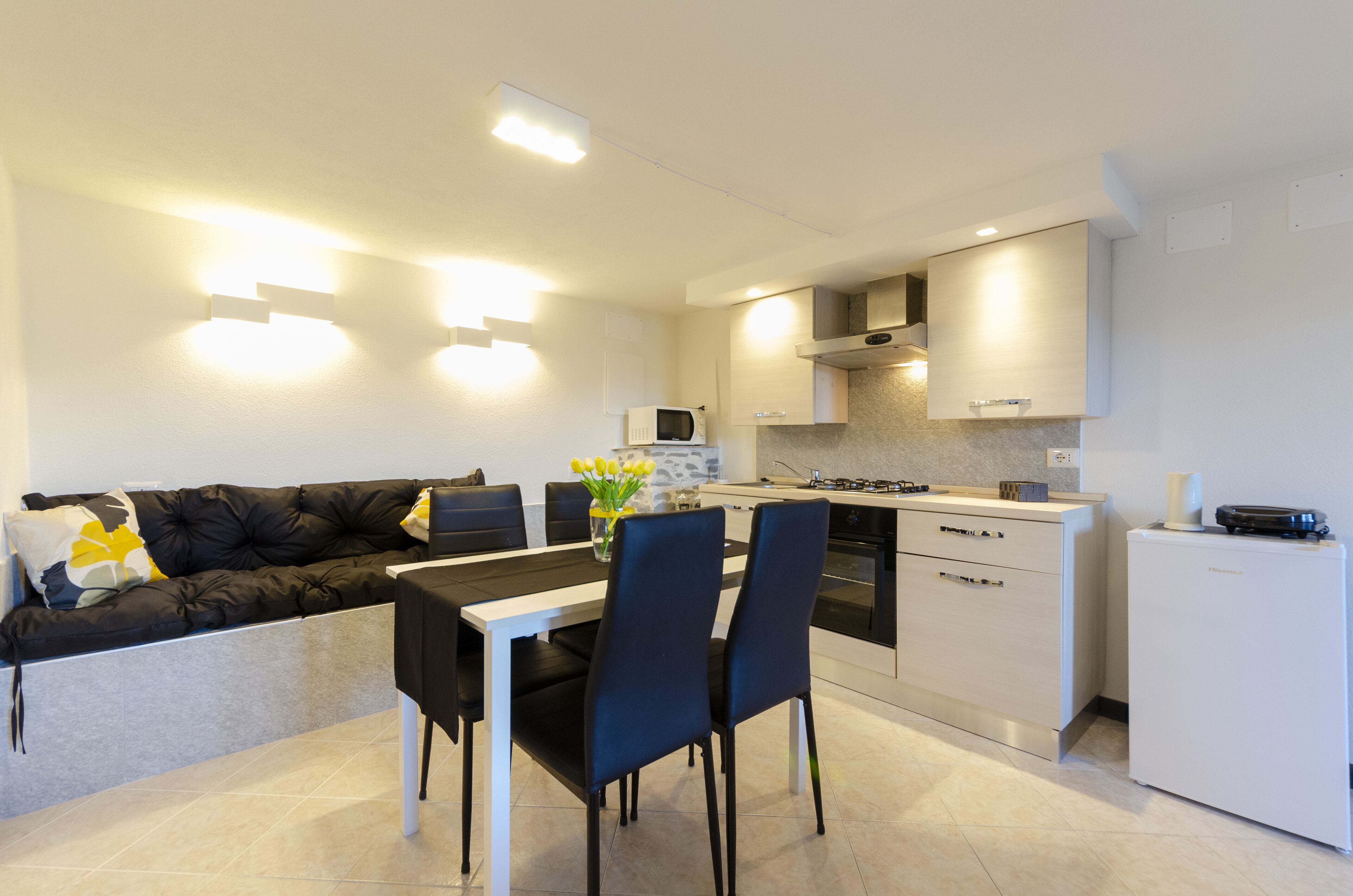 A modern kitchen with a dining area, white cabinets, a black sofa, and a small refrigerator.
