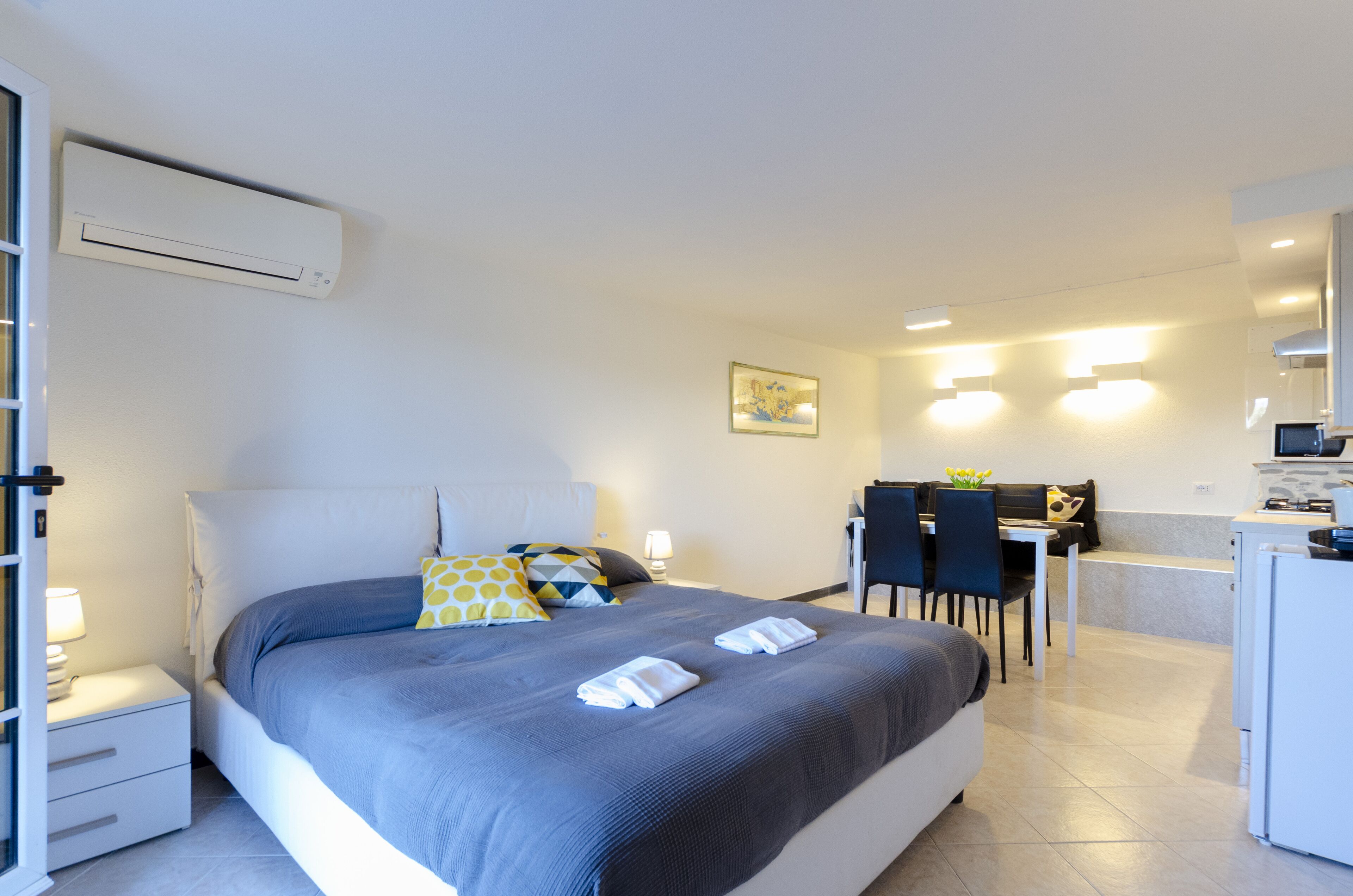A modern hotel room with a large bed, a desk, and a kitchenette.