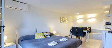 A modern hotel room with a large bed, a desk, and a kitchenette.