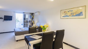 A modern hotel room with a bed, a dining area with a table and chairs, a flat-screen TV mounted on the wall, and a window with curtains. - Il Rifugio di San Massimo, Rapallo (Rapallo)