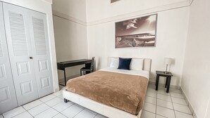 Una camera da letto con un letto, una scrivania, una sedia, un comodino, una lampada e una porta.