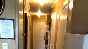 A narrow hallway with a patterned rug, a white door at the end, and a refrigerator on the right. - Steps from the Beach, sun, surf and boardwalk! (Corpus Christi)
