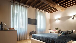Ein Schlafzimmer mit Bett, Schreibtisch, Stuhl, Fernseher und einem Fenster mit Vorhängen.