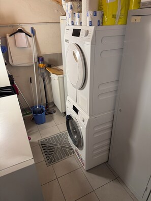 A laundry area with a front-loading washer and dryer, a mop, a bucket, and a vent.